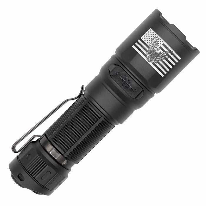 A black tactical flashlight with a metal clip, featuring an engraved American flag graphic with an eagle emblem on the head, shown against a plain white background.