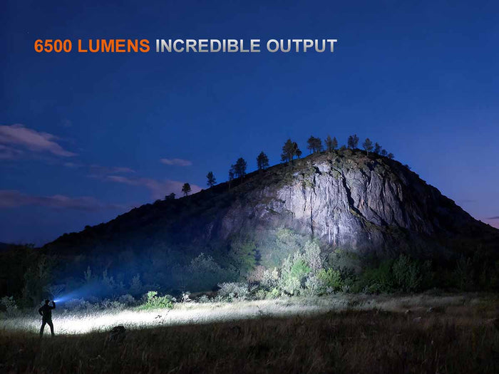Person using the TK28R tactical flashlight to illuminate a mountainous landscape with text about 6500 lumens output